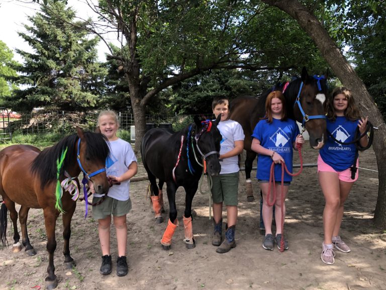 Group of kids participating in the Bravehearts program pose with horses.