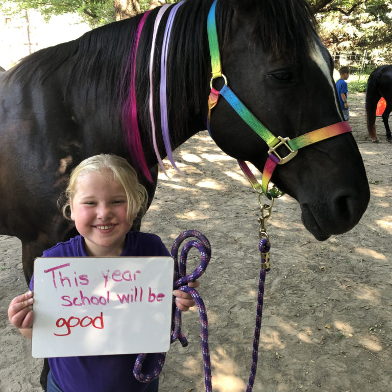 A girl holds up a hand-made thank you sign while standing in front of a horse. She is participating in Bravehearts equine program in Kearney, NE