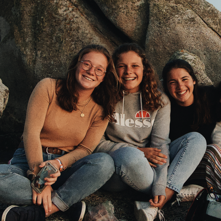 Three teen girls smile in front of rock.